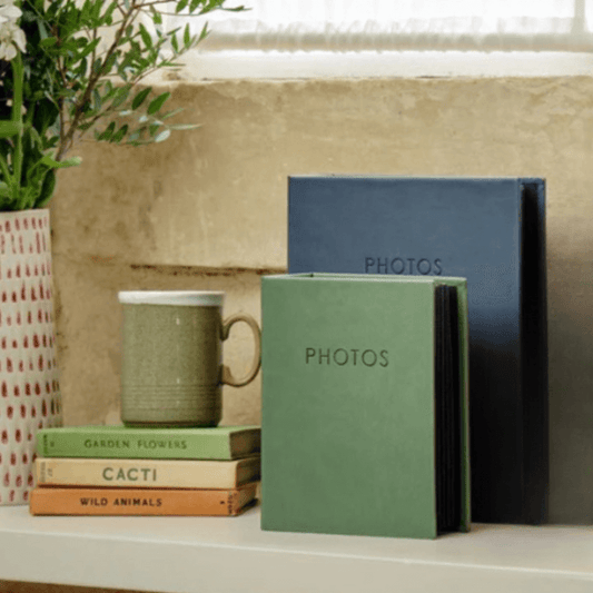 Stack of photo albums and a mug on a surface with a plant in the background. Fast delivery in Ireland.