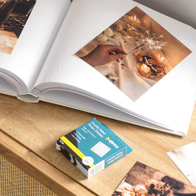 Open photo album with a box of photo stickers on a wooden surface