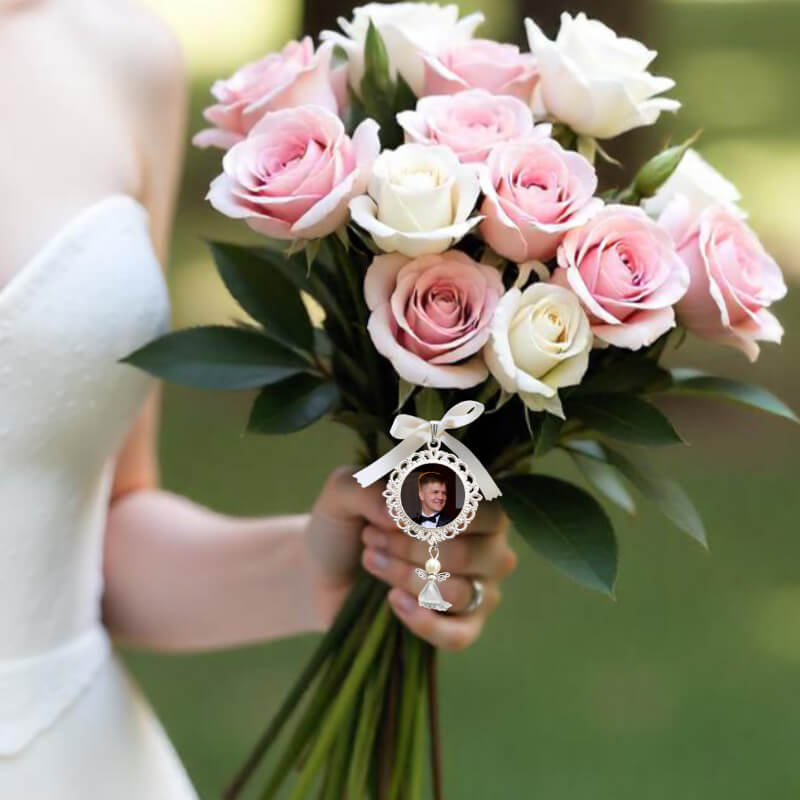 Bouquet of pink and white roses held by a person, with a decorative bridal bouquet charm featuring a photo of a loved one.