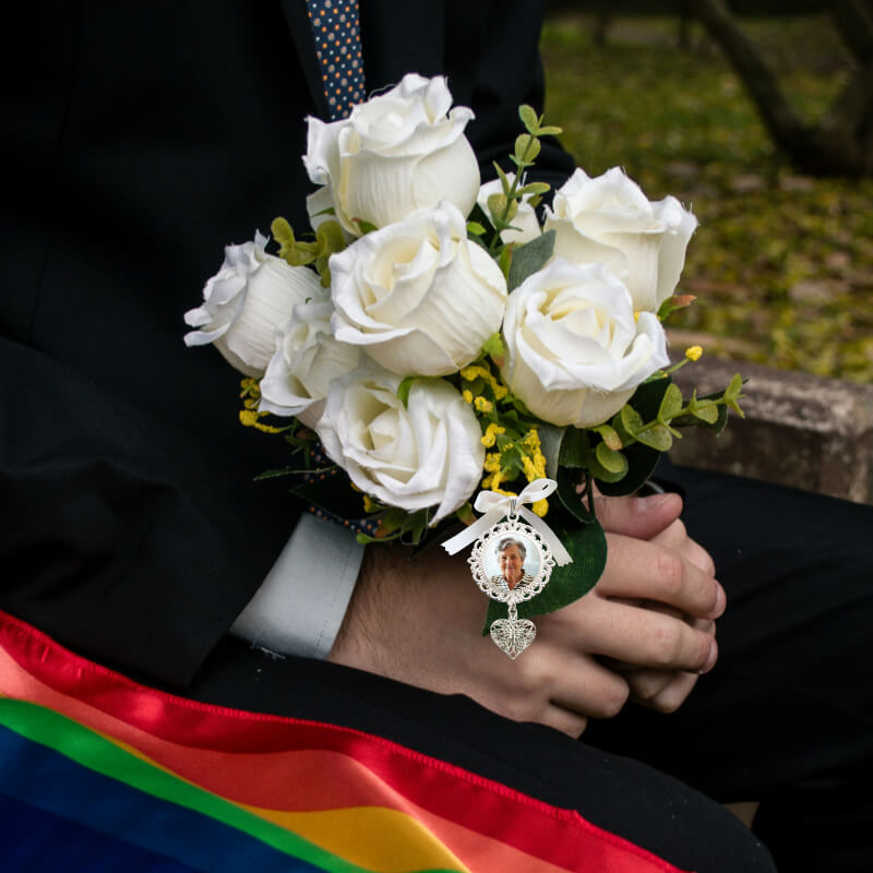 Person holding a bouquet of white roses with a rainbow sash and photo charm.
