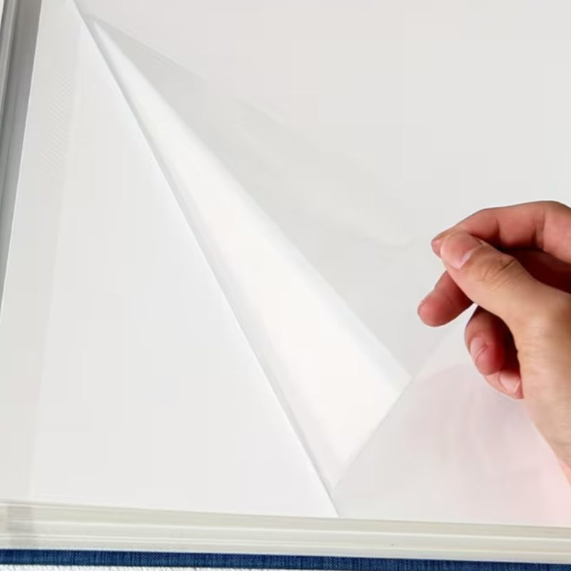 Self adhesive photo album page with peel back plastic covering. Hand holding a clear plastic sheet over a book with a white background